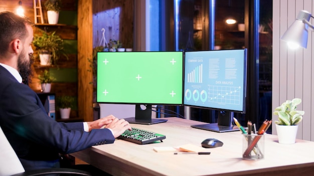 Biznesmen pracujący na dwóch monitorach, jeden z nich ma zielony ekran. Praca w nocy i światło księżyca