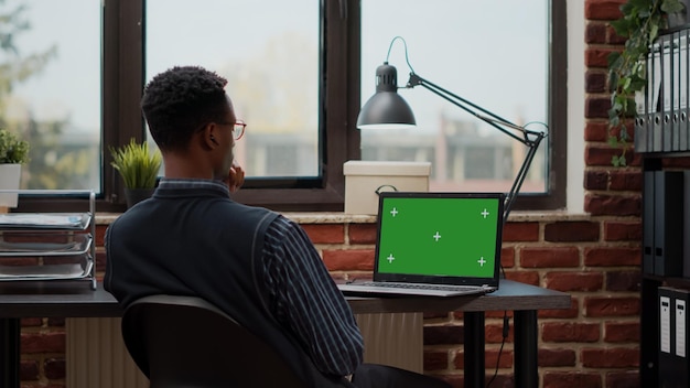 Biznesmen pracujący z laptopem i zielonym ekranem na wyświetlaczu, przy użyciu szablonu klucza chrominancji z makiety tła i izolowanej przestrzeni kopii. Pracownik firmy z pustym ekranem w biurze.