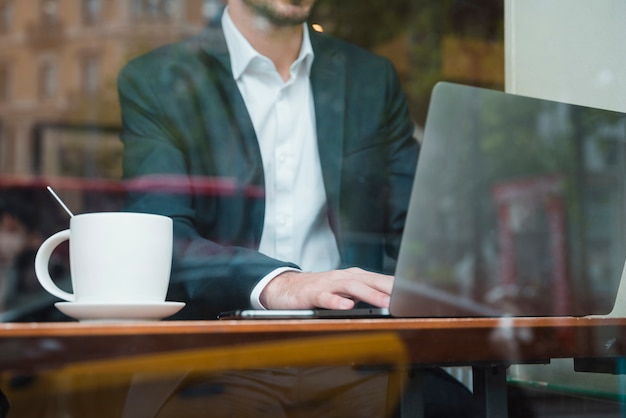 Bezpłatne zdjęcie biznesmen pracuje na laptopie w kawiarni widzieć przez szkła