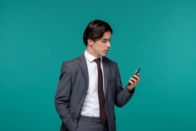 Biznesmen przystojny młody brunetka facet w szarym biurowym garniturze i krawacie, patrząc na ekran telefonu