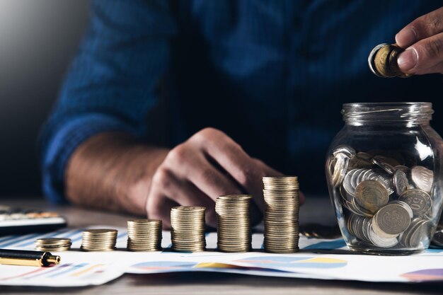 Biznesmen ręka trzyma monety wkładanie do słoika koncepcji finansów i rachunkowości oszczędności