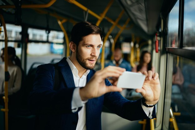 Biznesmen robi zdjęcie telefonem komórkowym podczas podróży autobusem publicznym