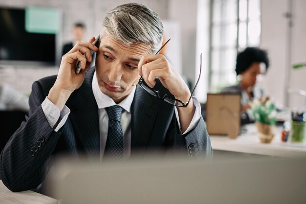 Biznesmen rozmawia przez telefon komórkowy siedząc przy biurku w biurze