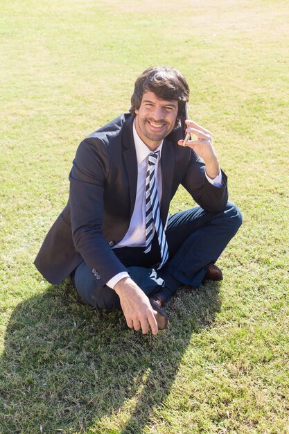 Biznesmen rozmawia przez telefon siedzi na trawie