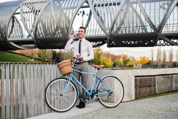 Biznesmen stojący przy swoim starym rowerze, mówiący przez telefon komórkowy