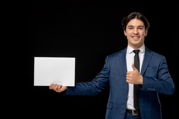 Bezpłatne zdjęcie biznesmen uroczy uroczy facet w ciemnoniebieskim garniturze z krawatem uśmiechający się z papierem