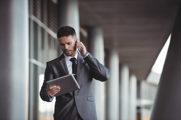 Biznesmen używa cyfrową pastylkę podczas gdy opowiadający na telefonie komórkowym