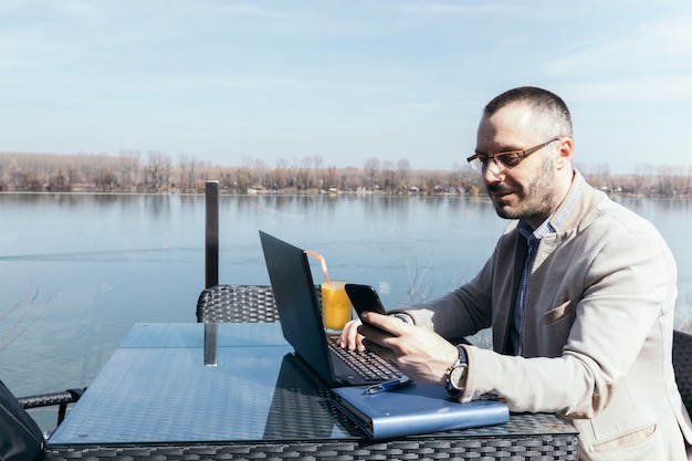 Bezpłatne zdjęcie biznesmen używa smartphone i laptop blisko nawadnia