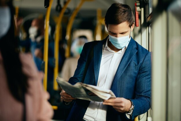 Biznesmen w masce ochronnej czyta gazetę podczas dojazdów autobusem