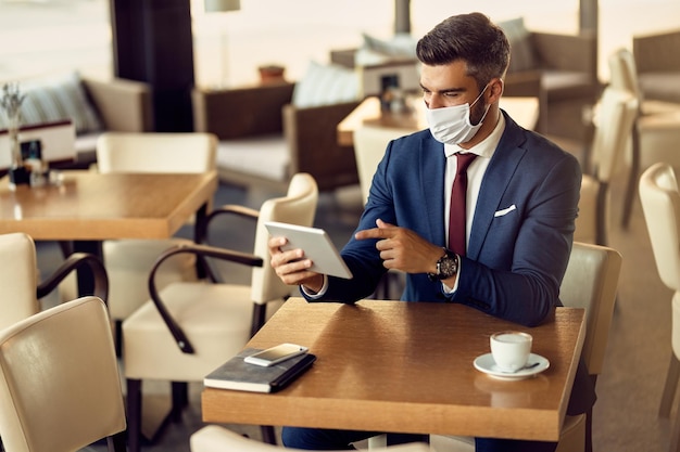 Biznesmen z maską ochronną za pomocą touchpada w kawiarni
