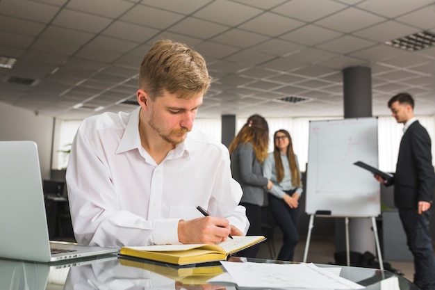 Bezpłatne zdjęcie biznesmena writing rozkład w dzienniczku z piórem przy miejscem pracy