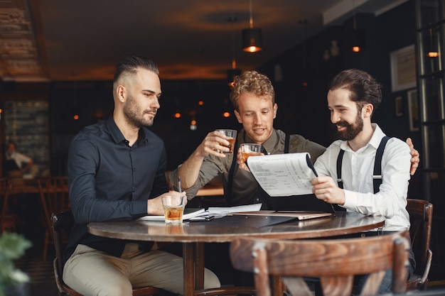 Biznesmeni w negocjacjach. Mężczyźni z alkoholem siedzący przy stole. Przyjaciele rozmawiają.