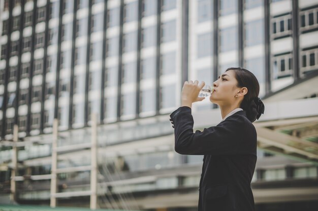 Biznesowa kobieta bierze spoczynkową wodę pitną przed centrum biznesu.