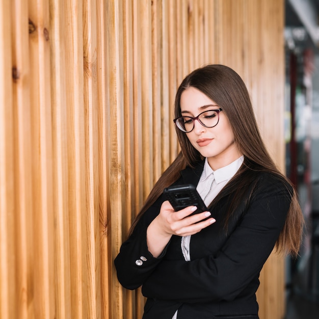 Bezpłatne zdjęcie biznesowa kobieta używa smartphone przy ścianą