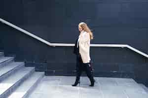 Bezpłatne zdjęcie biznesowa kobieta w płaszczu z torbą w rękach wchodzi po schodach do budynku. pojęcie kariery i biznesu