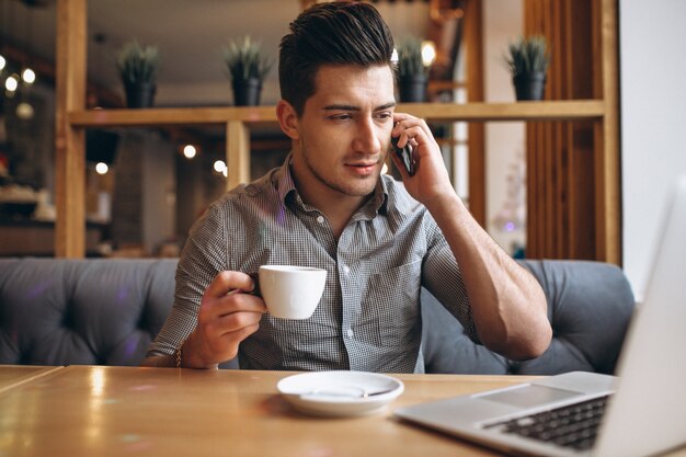 Biznesowy mężczyzna opowiada na telefonie i pije kawę w kawiarni