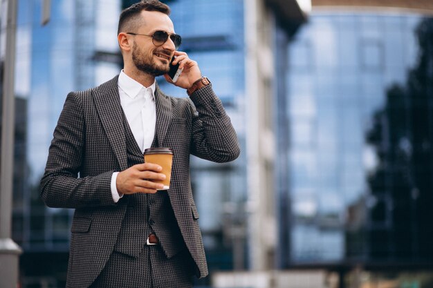 Biznesowy mężczyzna pije kawowego outside drapacz chmur z telefonem