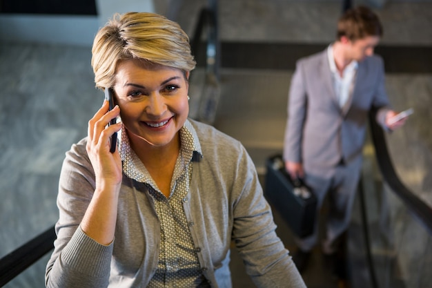 Bezpłatne zdjęcie bizneswoman opowiada na telefonie komórkowym na eskalatorze