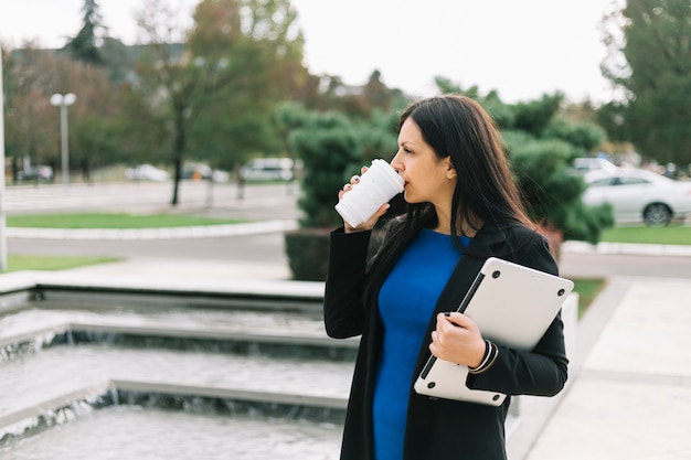 Bezpłatne zdjęcie bizneswoman pije kawę przy outdoors z laptopem