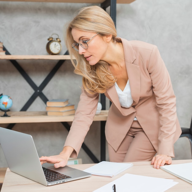 Bezpłatne zdjęcie bizneswoman pozycja przy miejscem pracy używać laptop
