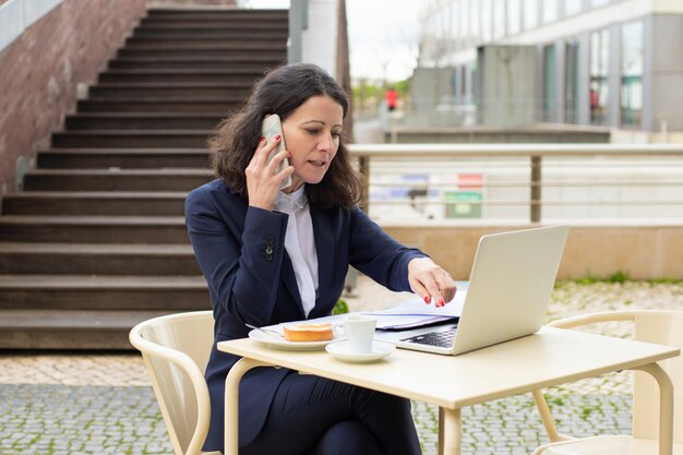 Bizneswoman używa laptop i smartphone w kawiarni