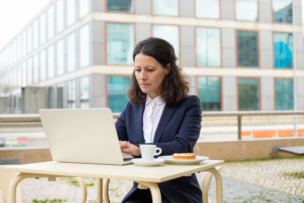 Bizneswoman używa laptop w plenerowej kawiarni