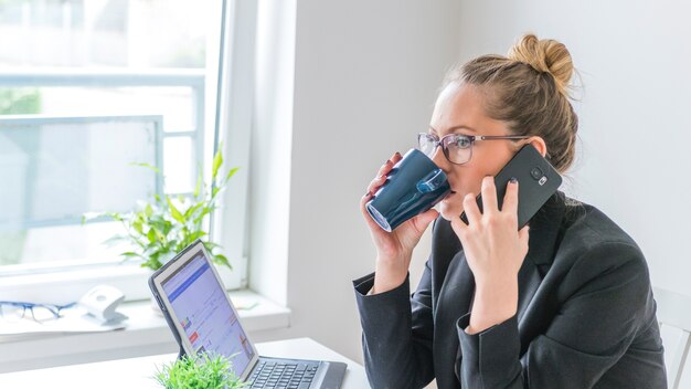 Bizneswoman używa telefon komórkowego podczas gdy pijący kawę
