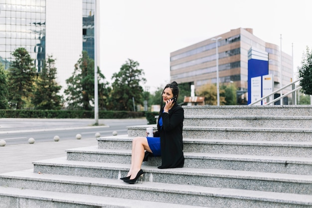 Bezpłatne zdjęcie bizneswomanu obsiadanie na schody opowiada na smartphone przy outdoors