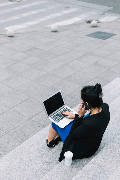 Bizneswomanu Obsiadanie Na Schody Używać Laptop I Opowiadać Na Telefonie Komórkowym