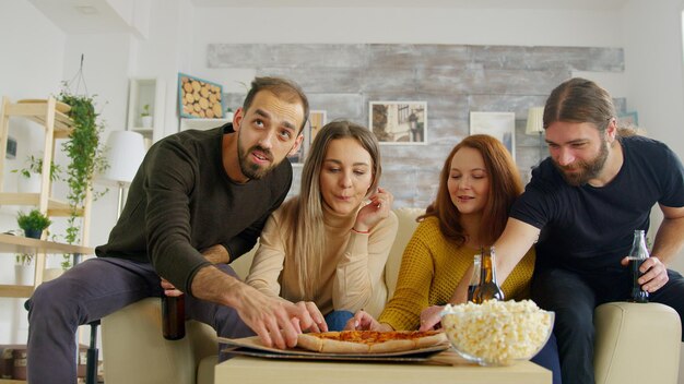 Bliscy przyjaciele oglądają telewizję w salonie, rozweselając się podczas oglądania meczu piłki nożnej na kanapie. Przyjaciele jedzą przekąski.