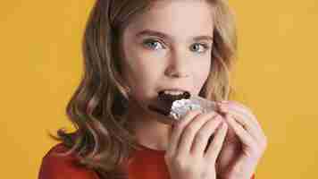 Bezpłatne zdjęcie bliska atrakcyjna blond nastolatka jedząca pyszną czekoladę na żółtym tle