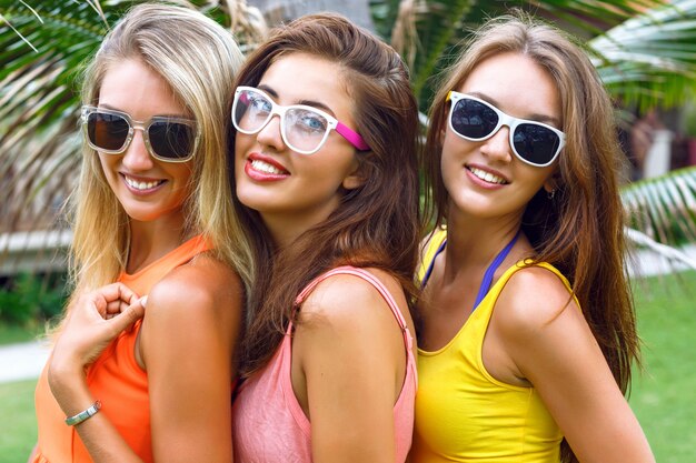 Bliska moda na zewnątrz portret jasny styl życia trzech młodych ładnych kobiet noszących jasne letnie sukienki i okulary przeciwsłoneczne. uśmiechnięty koniec ciesz się wakacjami.