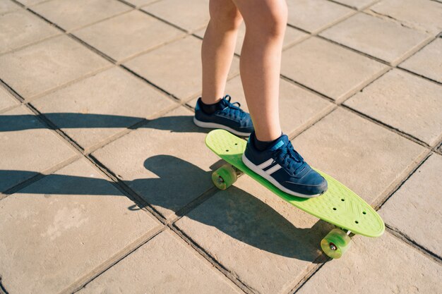 Bliska nogi w niebieskie trampki, jazda na zielonej deskorolce w ruchu. Aktywny miejski styl życia młodzieży, trening, hobby, aktywność. Aktywny sport na świeżym powietrzu dla dzieci. Dzieci na deskorolce.