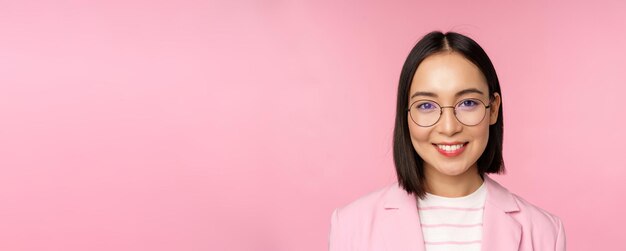 Bliska portret azjatyckiej kobiety korporacyjnej profesjonalnej bizneswoman w okularach uśmiechniętej i patrzącej pewnie na różowe tło aparatu