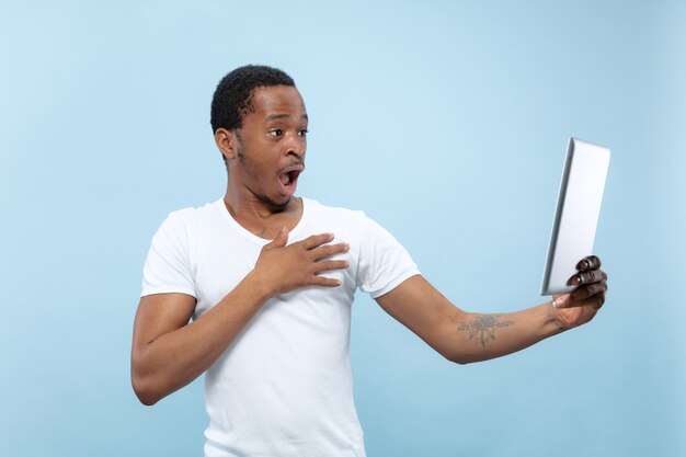 bliska portret młodego mężczyzny afro-amerykańskiego w białej koszuli. Ludzkie emocje, wyraz twarzy, reklama, koncepcja sprzedaży. Używając tabletu, w szoku. Robienie selfie lub vloga.
