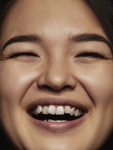Bliska portret młodej i emocjonalnej Chinki. Bardzo szczegółowe zdjęcie modelki o zadbanej skórze i jasnym wyrazie twarzy. Pojęcie ludzkich emocji. Uśmiecha się do kamery.