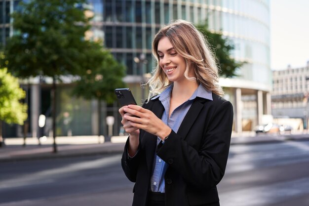 Bliska portret młodej kobiety korporacyjnej w czarnym garniturze trzyma wiadomość SMS na smartfonie, podczas gdy stan