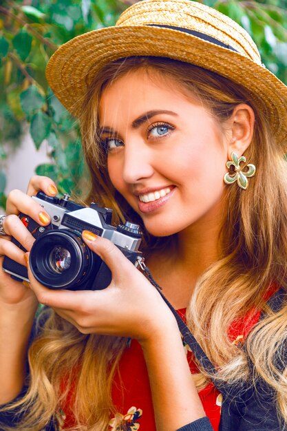 Bliska portret moda ładna blondynka młoda kobieta z naturalnym makijażem, na sobie słomkowy kapelusz, trzymając stary aparat starodawny retro hipster. Na dworze.