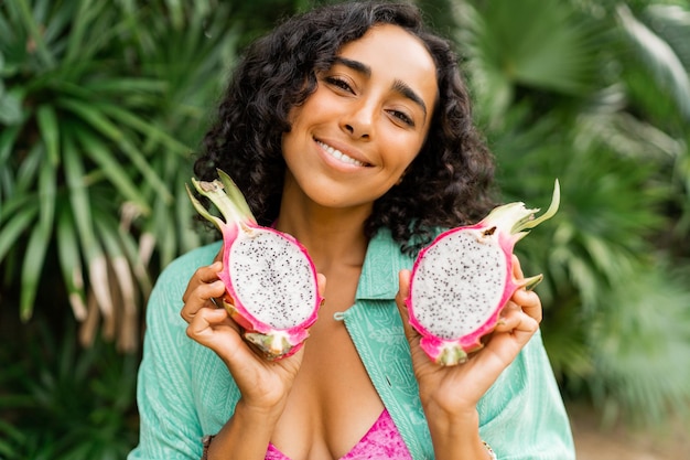 Bliska portret uśmiechniętej uroczej brunetki z falującymi włosami trzymającej owoce tropikalne