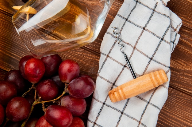 Bezpłatne zdjęcie bliska widok kieliszek białego wina i winogron z korkociągiem na tkaninie na drewnianym stole