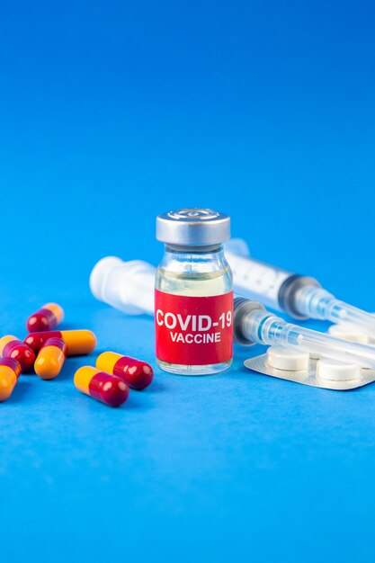 Bliski widok z przodu ampułki i kapsułek szczepionki COVID pakowanych w strzykawki z pigułkami na tle niebieskiej fali