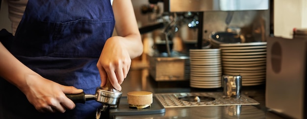 Bezpłatne zdjęcie blisko baristy kobiecych rąk tłoczących kawę w tamper przygotowuje porządek w kawiarni za ladą