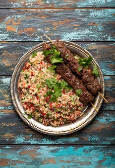 Bliskowschodnia turecka kolacja z mięsnym kebabem i tabbouleh sałatką z kuskus na rustykalnej metalowej płycie na drewnianym tle widok z góry, tradycyjny arabski posiłek