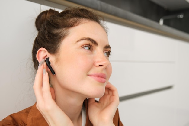 Bezpłatne zdjęcie bliższe zdjęcie młodej uśmiechniętej brunetki zakłada słuchawki i słucha muzyki w bezprzewodowym