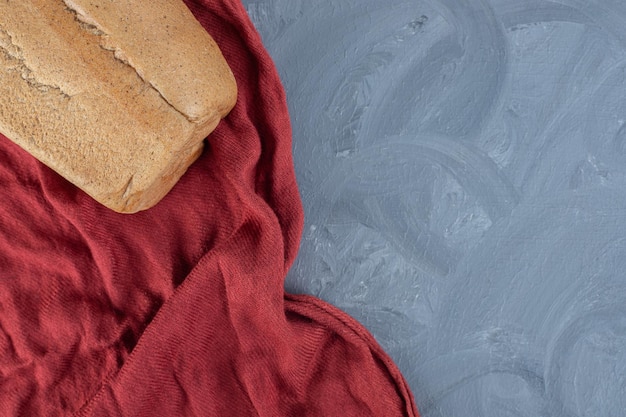 Bezpłatne zdjęcie blok chleba na pomarszczonym czerwonym obrusie na marmurowym stole.