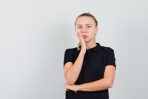 Blond dama stojąca w myślącej pozie w czarnej koszulce i smutny widok z przodu.