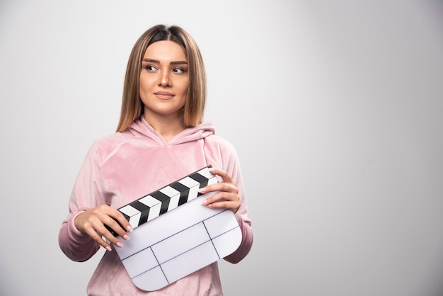 Bezpłatne zdjęcie blond dama w różowej bluzie trzyma pustą deskę klapy i daje naturalne pozy.