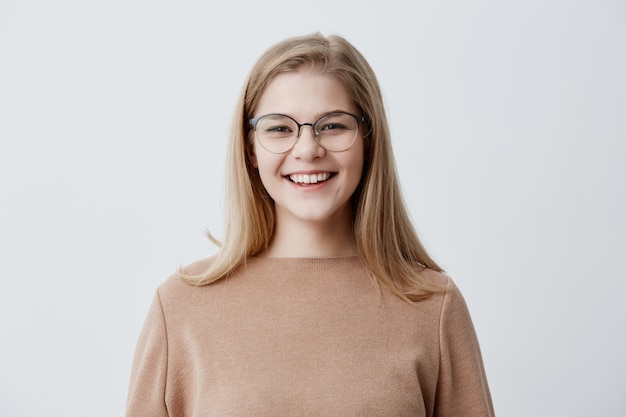 Blond figlarna młoda europejska kobieta ubrana w brązowy oversize'owy sweter, śmiejąca się z dobrego dowcipu, demonstrująca idealnie białe zęby, a jej wygląd i wyraz twarzy były pełne radości i szczęścia. Ludzie i styl życia