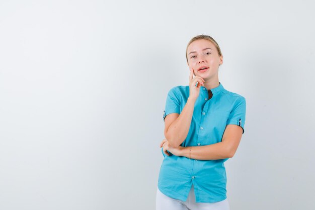 Blond kobieta podpierająca podbródek w niebieskiej bluzce i wyglądająca wesoło na białym tle