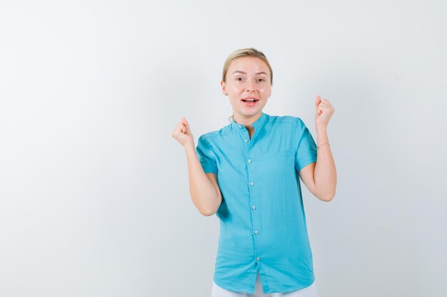 Blond kobieta pokazuje gest zwycięzcy w niebieskiej bluzce i wygląda na szczęśliwą